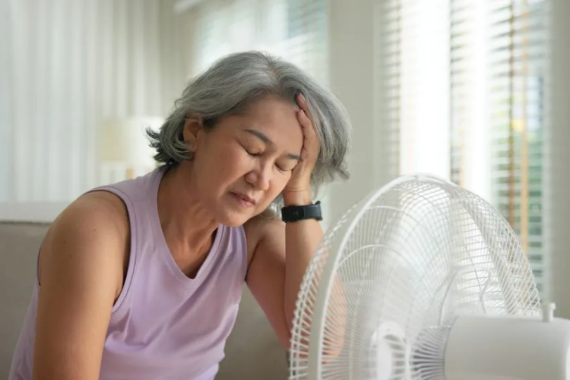 A woman sitting in front of a fan with her head in her hands. 